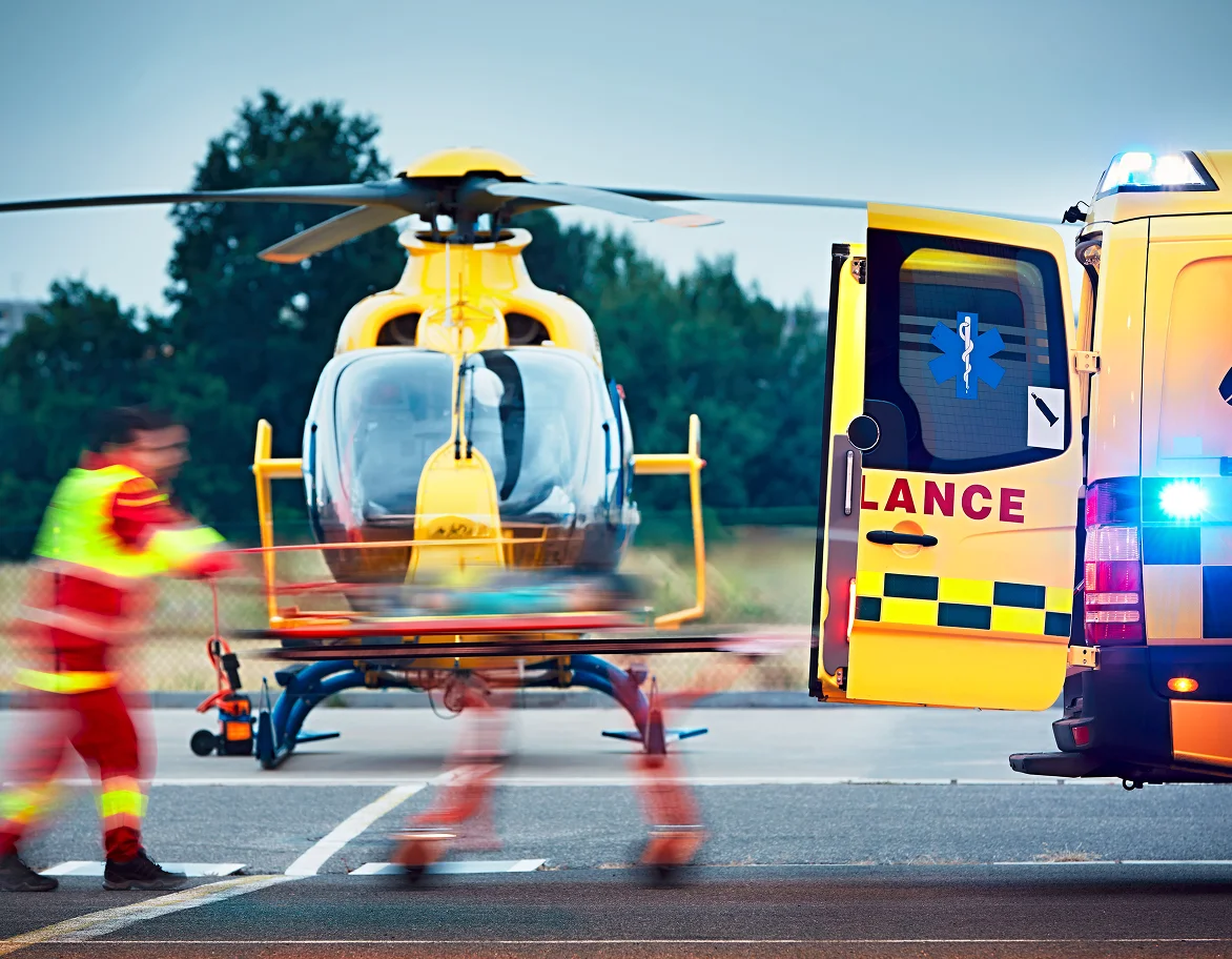 Medical air ambulance helicopter with emergency responders on tarmac next to ambulance vehicle with active emergency lights